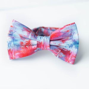 Peut inclure: Un nœud papillon avec un motif abstrait bleu et rose. Le nœud papillon est en tissu et a une forme classique.