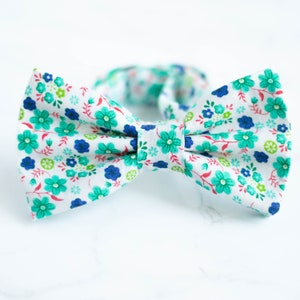 May include: A white bow tie with a floral pattern in shades of blue, green, and pink.