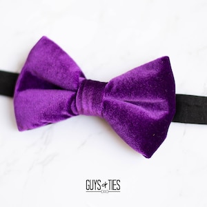 May include: A purple velvet bow tie with a black adjustable strap.  The bow tie is on a white marble surface.  Guys + Ties.com