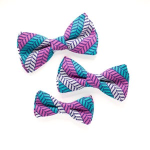 May include: Three bow ties in different sizes, all with a pink, white, and teal geometric pattern.