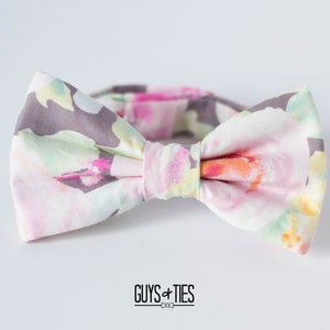 May include: A bow tie with a floral pattern in shades of pink, green, and gray. The bow tie is tied and ready to wear.