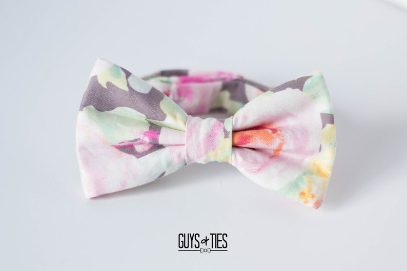May include: A bow tie with a floral pattern in shades of pink, green, and gray. The bow tie is tied and ready to wear.