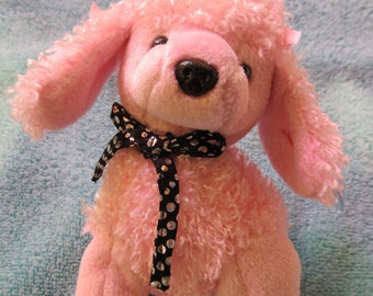May include: Pink plush poodle toy with a black and white polka dot bow. The toy has a curly, fluffy texture.