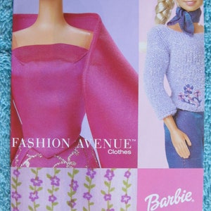 May include: A pink and purple Barbie doll clothing packaging with the text "Fashion Avenue Clothes" and "Barbie". The packaging features two Barbie dolls wearing different outfits. One doll is wearing a pink dress with a floral pattern and the other doll is wearing a lavender sweater and blue jeans.