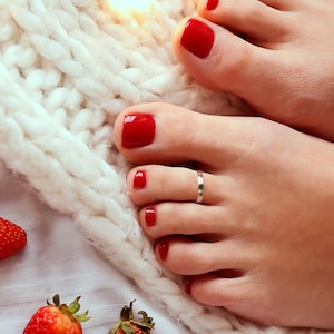 May include: Close-up of a woman's feet with red nail polish and a silver toe ring. The feet are resting on a white knitted blanket.