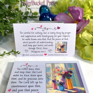 Pode incluir: Dois cart&otilde;es brancos com obras de arte florais e vers&iacute;culos b&iacute;blicos. Um cart&atilde;o apresenta Filipenses 4:6-7, o outro N&uacute;meros 6:24-26. Os cart&otilde;es s&atilde;o cercados por flores e vegeta&ccedil;&atilde;o, com um objeto decorativo azul ao fundo.