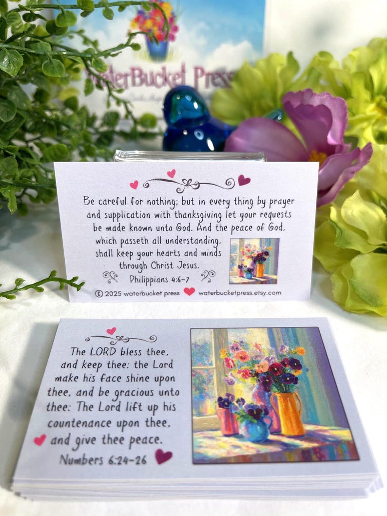 Pode incluir: Dois cart&otilde;es brancos com obras de arte florais e vers&iacute;culos b&iacute;blicos. Um cart&atilde;o apresenta Filipenses 4:6-7, o outro N&uacute;meros 6:24-26. Os cart&otilde;es s&atilde;o cercados por flores e vegeta&ccedil;&atilde;o, com um objeto decorativo azul ao fundo.