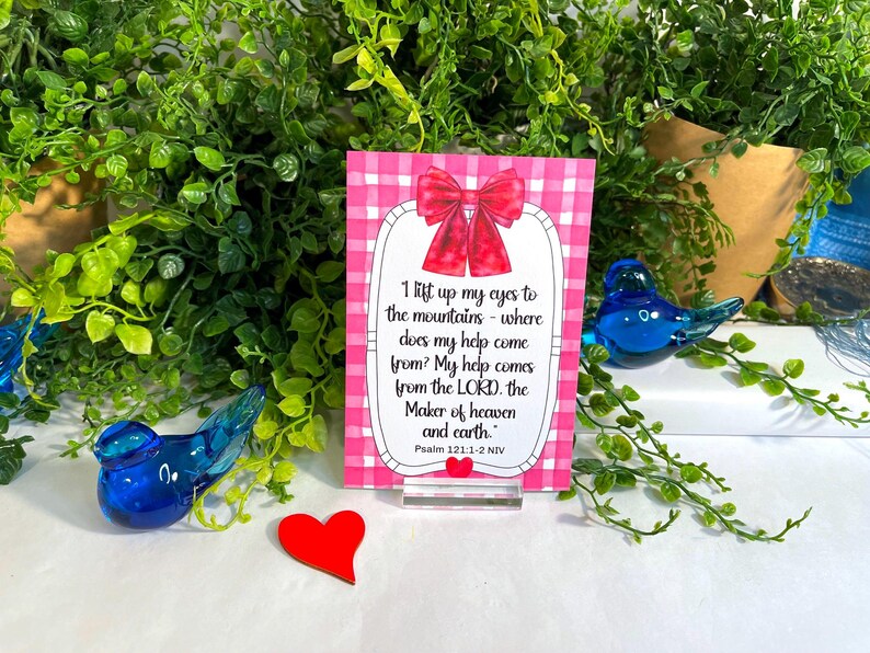 K&ouml;nnte beinhalten: Eine rechteckige Karte mit einem rosa-wei&szlig;en Vichy-Muster, einer roten Schleife oben und einem kleinen roten Herz unten. Der Text lautet: I lift up my eyes to the mountains - where does my help come from? My help comes from the LORD, the Maker of heaven and earth. Psalm 121:1-2 NIV.