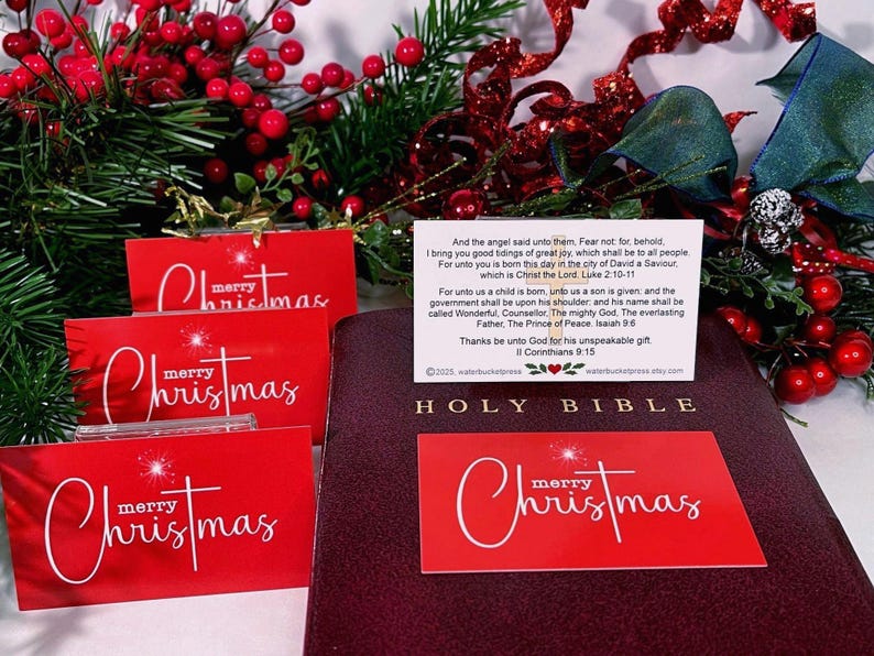 Peut inclure: Cartes de No&euml;l rouges avec l'inscription "merry Christmas" en blanc. Une Sainte Bible bordeaux et des d&eacute;corations festives avec des baies rouges et des rubans sont en arri&egrave;re-plan. Une petite carte avec du texte est &eacute;galement pr&eacute;sente.