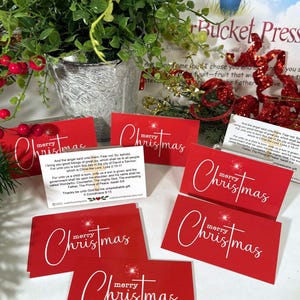 Peut inclure: Cartes de No&euml;l rouges avec l'inscription blanche &laquo;&nbsp;merry Christmas&nbsp;&raquo;. Les cartes rectangulaires pr&eacute;sentent un motif d'&eacute;clat d'&eacute;toile. Un pot de plante et des d&eacute;corations festives sont en arri&egrave;re-plan.