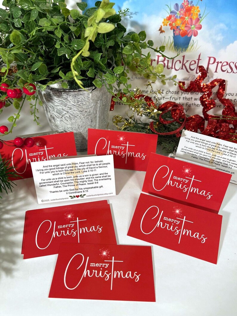 Peut inclure: Cartes de No&euml;l rouges avec l'inscription blanche &laquo;&nbsp;merry Christmas&nbsp;&raquo;. Les cartes rectangulaires pr&eacute;sentent un motif d'&eacute;clat d'&eacute;toile. Un pot de plante et des d&eacute;corations festives sont en arri&egrave;re-plan.
