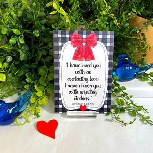 K&ouml;nnte beinhalten: Ein rechteckiges Schild mit schwarz-wei&szlig;em Karomuster, einer roten Schleife oben und einem wei&szlig;en Mittelfeld mit dem Text: I have loved you with an everlasting love: I have drawn you with unfailing kindness. Jeremiah 31:3 NIV.