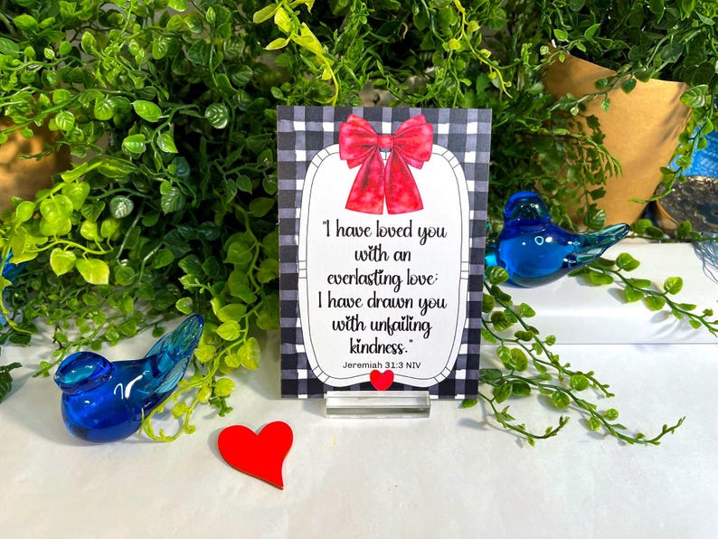 K&ouml;nnte beinhalten: Ein rechteckiges Schild mit schwarz-wei&szlig;em Karomuster, einer roten Schleife oben und einem wei&szlig;en Mittelfeld mit dem Text: I have loved you with an everlasting love: I have drawn you with unfailing kindness. Jeremiah 31:3 NIV.