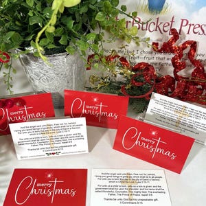 Peut inclure: Cartes de No&euml;l rouges avec l'inscription blanche &laquo; joyeux No&euml;l &raquo; et un motif en forme d'&eacute;clat d'&eacute;toile. Chaque carte comprend un verset biblique. Les cartes sont dispos&eacute;es avec de la verdure et des &eacute;l&eacute;ments d&eacute;coratifs.