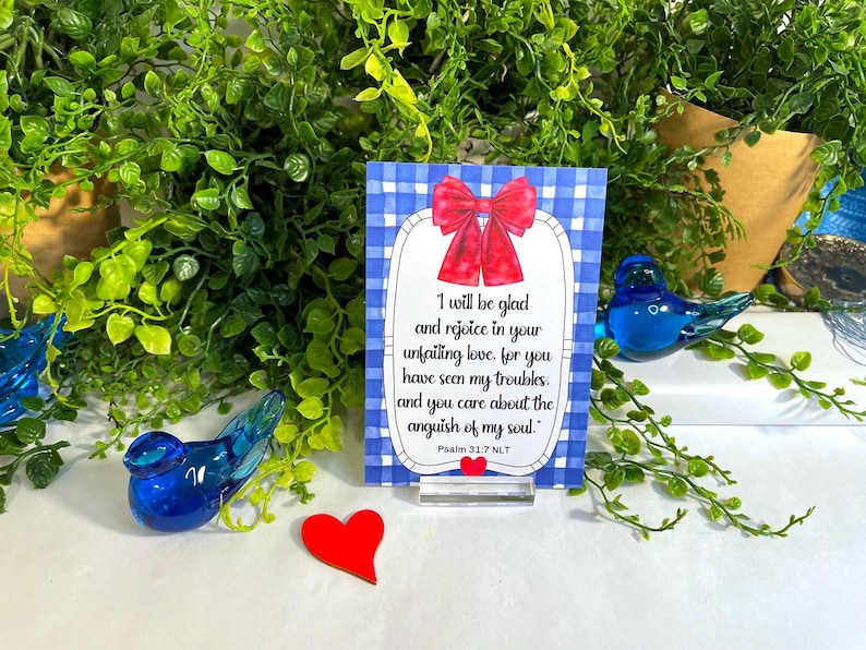 K&ouml;nnte beinhalten: Eine rechteckige Karte mit blau-wei&szlig;em Vichy-Muster, verziert mit einer roten Schleife oben und einem kleinen roten Herz unten. Der Text lautet: I will be glad and rejoice in your unfailing love, for you have seen my troubles, and you care about the anguish of my soul. Psalm 31:7 NLT.