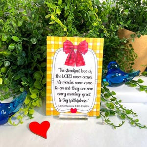 K&ouml;nnte beinhalten: Eine rechteckige Karte mit gelb-wei&szlig;em Vichy-Muster, verziert mit einer roten Schleife oben und einem kleinen roten Herz unten. Der Text lautet: The steadfast love of the LORD never ceases, his mercies never come to an end; they are new every morning: great is thy faithfulness. Lamentations 3:22-23 RSV.