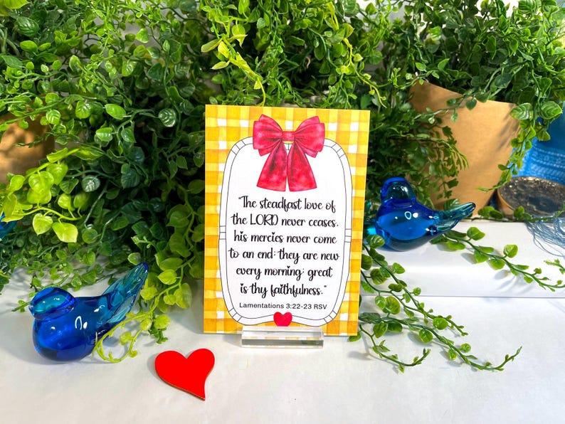 K&ouml;nnte beinhalten: Eine rechteckige Karte mit gelb-wei&szlig;em Vichy-Muster, verziert mit einer roten Schleife oben und einem kleinen roten Herz unten. Der Text lautet: The steadfast love of the LORD never ceases, his mercies never come to an end; they are new every morning: great is thy faithfulness. Lamentations 3:22-23 RSV.