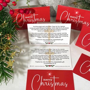Peut inclure: Cartes de No&euml;l rouges avec l'inscription "merry Christmas" en blanc. Les cartes comportent un encart blanc avec un texte religieux. Des feuilles vertes et des baies rouges sont en arri&egrave;re-plan. Un article de vacances festif.