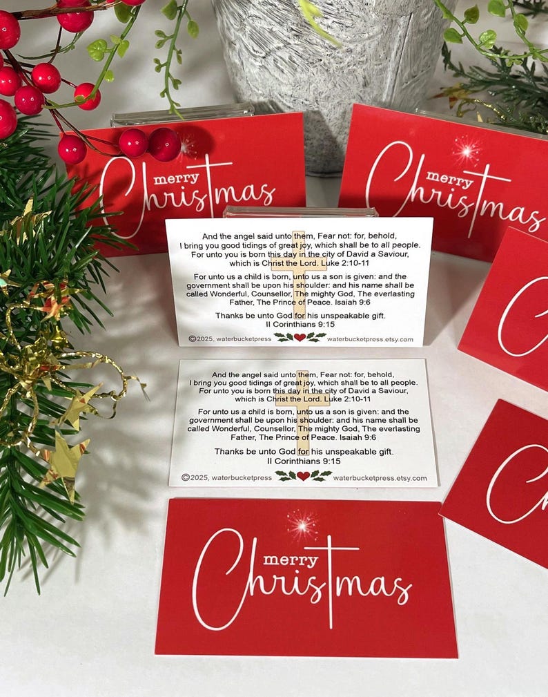 Peut inclure: Cartes de No&euml;l rouges avec l'inscription "merry Christmas" en blanc. Les cartes comportent un encart blanc avec un texte religieux. Des feuilles vertes et des baies rouges sont en arri&egrave;re-plan. Un article de vacances festif.