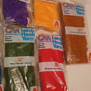 May include: Six packages of Columbia-Minerva latch hook yarn in various colors, including purple, orange, copper, green, red, and a light brown. Each package contains 320 pieces and weighs 0.7 ounces. The packages are labeled with the color name and number, and the words "Latch Hook Yarn" and "Always the exact same color."