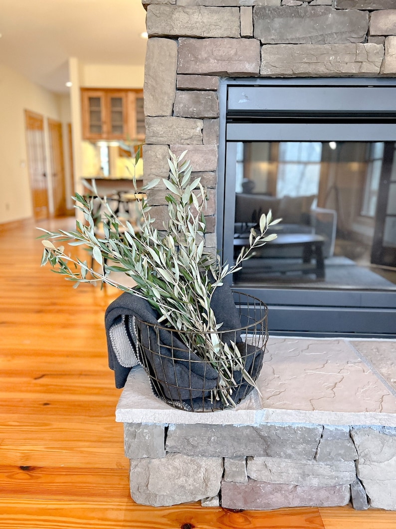 May include: A gray blanket in a wire basket with green branches on a stone fireplace mantel.
