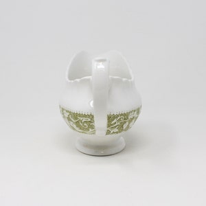 May include: White ceramic gravy boat with a green floral design. The boat has a scalloped edge and a handle.
