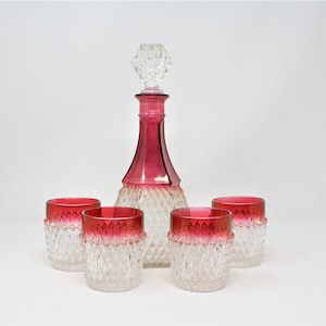May include: A set of four clear glass tumblers with a diamond pattern and a red base, and a matching decanter with a clear glass body and a red base.