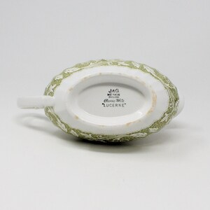 May include: A white ceramic gravy boat with a green floral pattern. The bottom of the boat has the text "JAG MEAKIN ENGLAND Classic Ware 'LUCERNE'" printed on it.