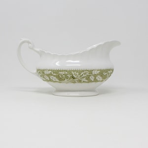 May include: A white ceramic gravy boat with a green floral design around the rim.