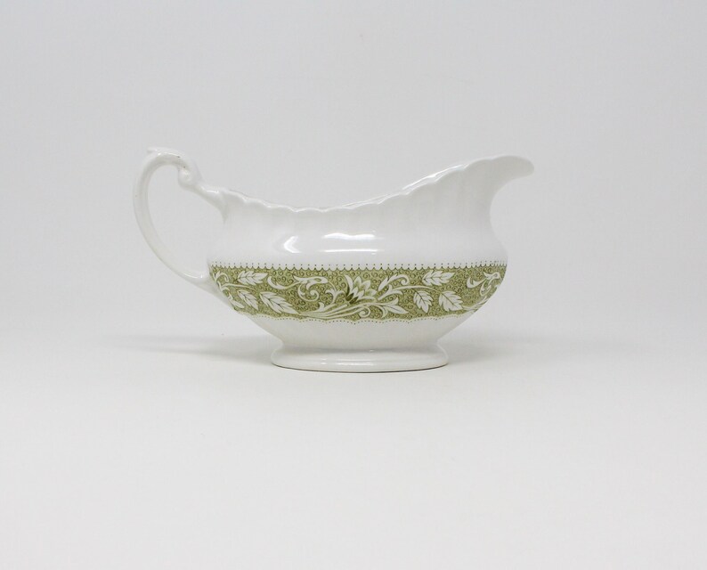 May include: A white ceramic gravy boat with a green floral design around the rim.