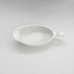 May include: White ceramic gravy boat with a handle. The boat is empty and ready to be filled with gravy or sauce.