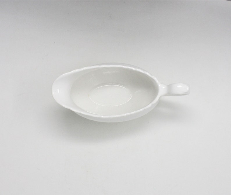 May include: White ceramic gravy boat with a handle. The boat is empty and ready to be filled with gravy or sauce.