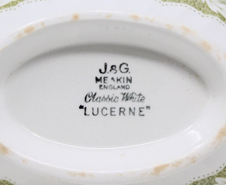 May include: Close-up of the bottom of a white ceramic dish with a green floral pattern. The dish is marked "J&G. MEAKIN ENGLAND Classic White "LUCERNE""