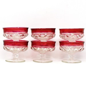 May include: Set of six clear glass stemmed dessert cups with a red rim. The cups have a textured design and are perfect for serving ice cream, pudding, or other desserts.