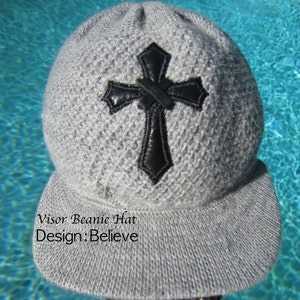 May include: Gray beanie hat with a black cross design and a visor. The hat has the text "Visor Beanie Hat Design: Believe" on the front.