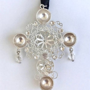 May include: A silver filigree cross pendant with four round, hollowed-out sections and crystal accents hanging from the bottom.