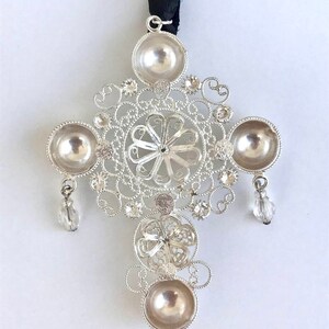 May include: A silver filigree cross pendant with four round, hollowed-out sections and crystal accents hanging from the bottom.