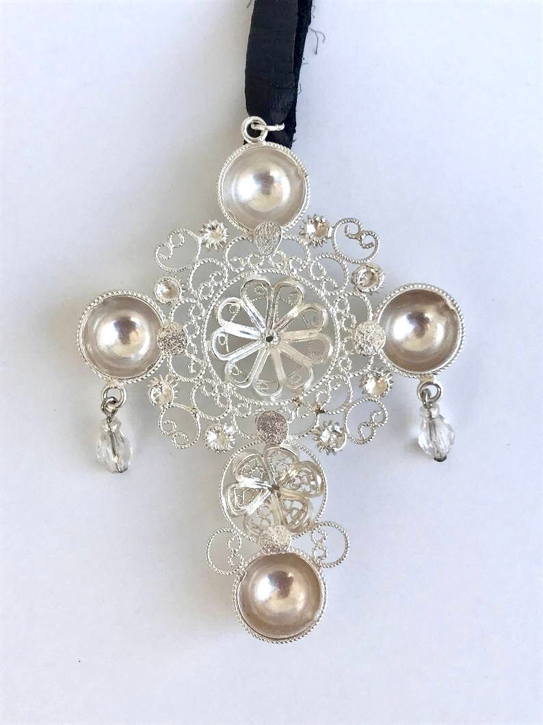 May include: A silver filigree cross pendant with four round, hollowed-out sections and crystal accents hanging from the bottom.