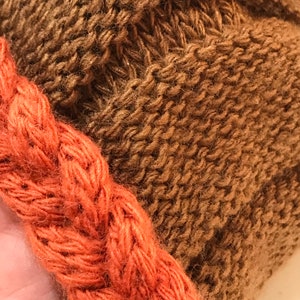 May include: A brown knitted hat with a thick orange braided trim.