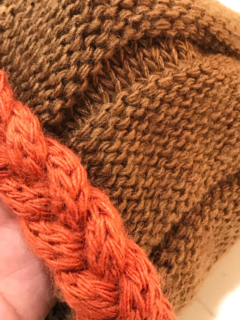 May include: A brown knitted hat with a thick orange braided trim.