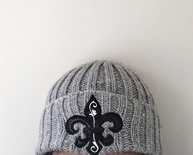 May include: Grey knitted beanie with a black and white fleur-de-lis emblem.