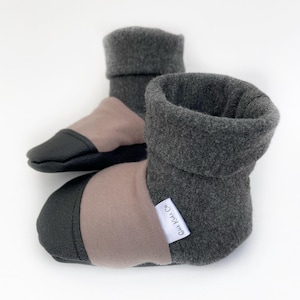 May include: A pair of gray and brown baby booties with a black leather sole. The booties have a fold-over cuff and a white label that says "Gull Kida Co."