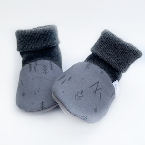 May include: Gray baby booties with a forest print. The booties have a fold-over cuff and a soft, textured fabric.