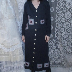 Peut inclure: Une robe longue noire à manches longues avec un devant boutonné et un motif patchwork orné de petits papillons rouges et noirs. La robe est portée par une personne debout devant un rideau de dentelle blanche.
