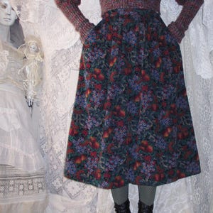 May include: A two-piece outfit featuring a burgundy knit sweater and a floral print skirt. The skirt has a dark background with red and purple floral patterns. The outfit is paired with black boots.