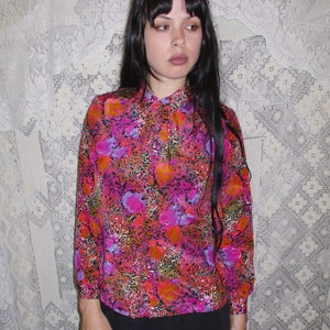 80s blouse with pleats in front and a pattern of bright floral and scribble pattern of  orange, pink, purple, green, white, and mustard yellow