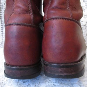 May include: Close-up of two brown leather boots. The boots have a worn appearance with visible scuffs and creases. The soles are dark brown and show signs of wear. The boots appear to be vintage or well-used, with a classic design.