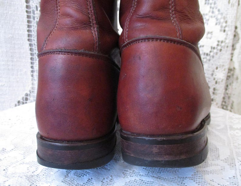 May include: Close-up of two brown leather boots. The boots have a worn appearance with visible scuffs and creases. The soles are dark brown and show signs of wear. The boots appear to be vintage or well-used, with a classic design.