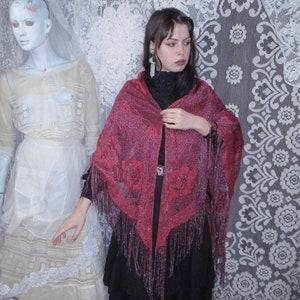 Pink Sparkly floral fringed shawl worn by a woman in all black, a long skirt and blouse, and dark hair parted to the side  with a bobby pin. A sixties mannequin wearing layers of antique white clothing is in the background, along with white lace.
