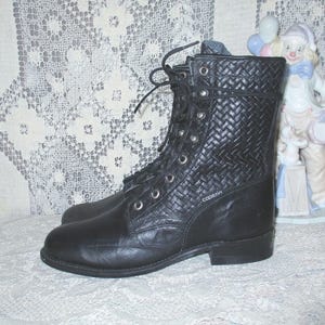 May include: Black leather lace-up boots with a woven pattern. The boots have a rounded toe and a chunky heel. The brand name "Cobian" is visible on the side of the boot.